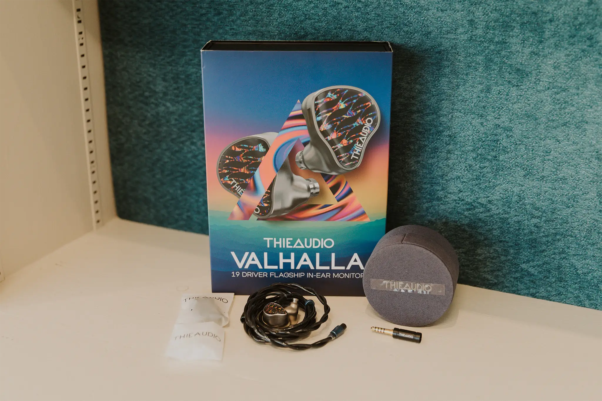 Thieaudio Valhalla box with the earphones on a black cable, round case, spare plug and pouches